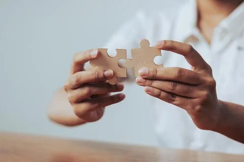 Womans hands delicately join two puzzle pieces on a rustic wooden table sho.. Stock Photos