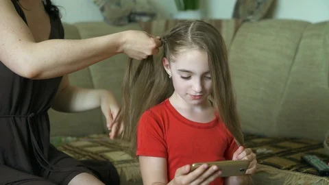 Woman's hands do hairstyle for her little daughter. A woman is braiding hair for Stock Footage 90607287