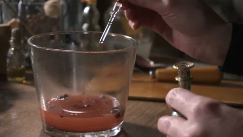 Woman's hands drip some substance into the glass with red liquid Stockbeeldmateriaal 89675018