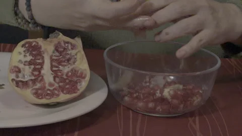 Woman's hands extracting fresh pomegranate seeds into glass bowl Video stock 321751942