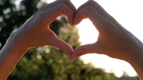 Womans Hands fold heart. The rays of the sun shine through the heart at sunset Stock Footage 135052752