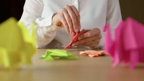 Woman's hands folding origami colored paper on table. Hobby Stock Footage 296903257