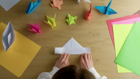 Woman's hands folding origami colored paper on table. Hobby Stock Footage 296903432