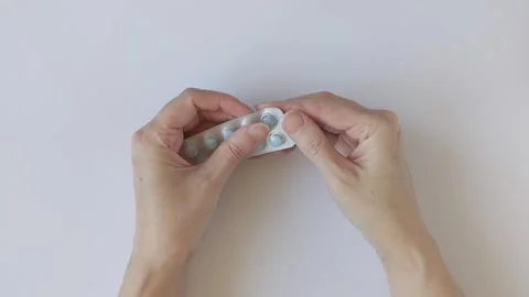 Woman's hands gently press on a blister pack with pills Stock Footage 337948574