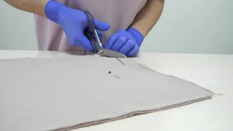 Woman's hands in gloves cutting a beige fabric with scissors on table in atelier Stock Footage 157213568