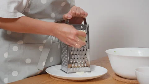 A woman's hands grating a block of hard cheese on a metal box grater 스톡 동영상 315596303