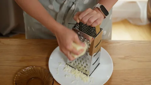 A woman's hands grating a block of mozzarella cheese on a box grater Stock Footage 315905571