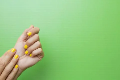 A woman's hands with her nails painted yellow on a green background. Stock Photos