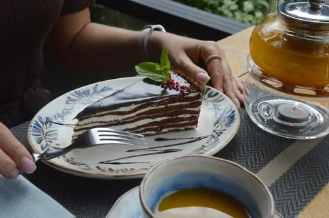 A woman's hands hold a fork and a plate with a piece of cake on a table in a Stock Photos