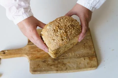Woman's hands hold fresh bread on a wooden board. Stock Photos