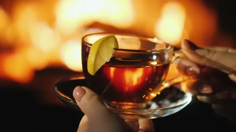 Woman's hands hold transparent teacup with lemon slice, fire and bokeh glow.. Stock Footage 334993008