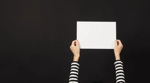 Woman's hands is holding blank empty the A4 paper on black background.woman w Stock Photos