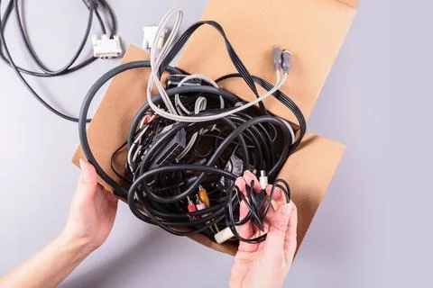 Woman's hands holding electronic cables next to cardboard box Foto stock