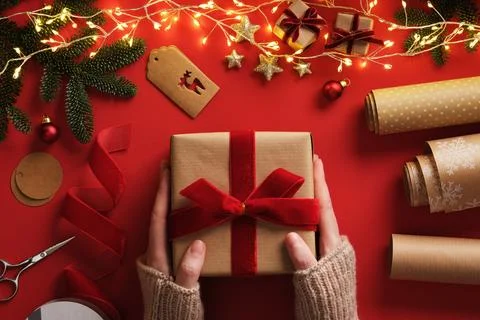 A woman's hands holding a gift. Table with handmade supplies, rolls of kraf.. Foto stock