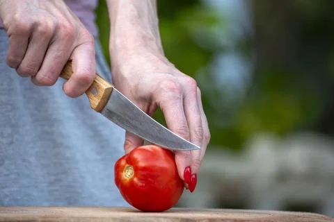 Woman's hands holding a sharp kitchen knife, preparing to slice a ripe, red.. Stock Photos