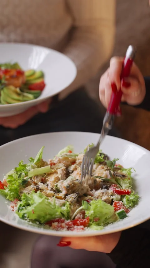 Womans hands holding a white plate and mixing a fresh Caesar salad with a fork Stock Footage 328531969