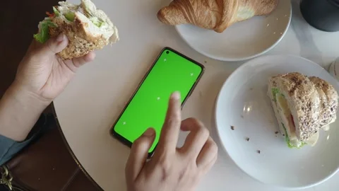 Woman's hands interact with green screen smartphone during meal in cafe, ov.. Stock Footage 332578333