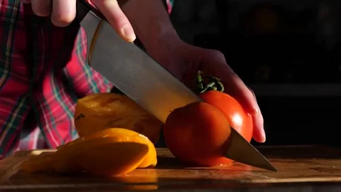Woman's hands in kitchen cutting fresh tomato on wooden cutting board Stock-Footage 147934917