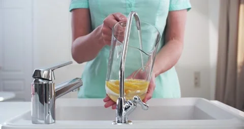 Woman’s hands in the kitchen draw filtered water in a jug with lemons. Vidéo 230644734