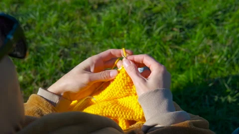 Woman's hands knitting yellow yarn outdoors on green grass. Stock Footage 332645364
