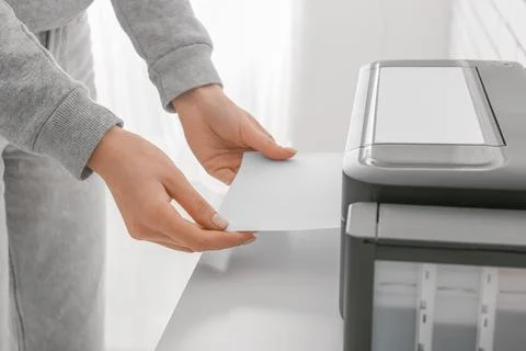 Womans hands loading white paper into a modern printer for home office docume Stock Photos