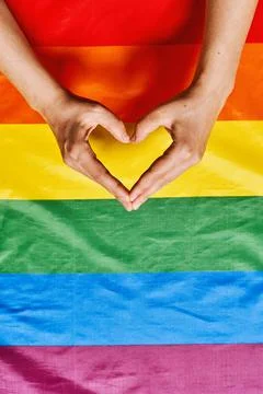 Womans hands making heart shape over the lgbtq rainbow flag background Stock Photos