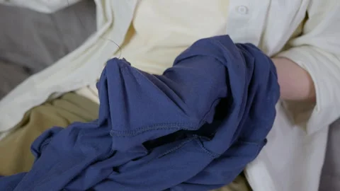 Woman's hands mending blue clothes with needle Stock Footage 345419672