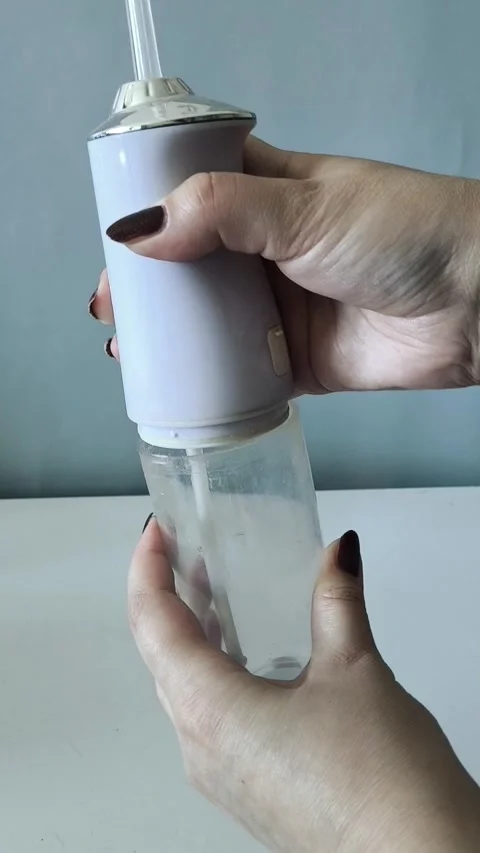 A womans hands open the irrigator to pour water into a glass. Using an irrigator Vidéo 329969593