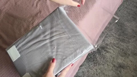 A womans hands open a package with a new sheet with an elastic band against the Stock Footage 327457033