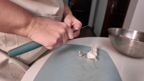 A womans hands peel garlic with a knife over a cutting board Stock Footage 319372196