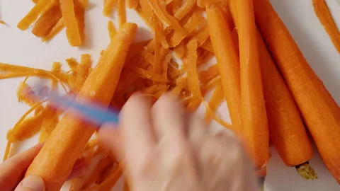 Woman's hands peeling carrots using a peeler knife, close-up view Video stock 265600069