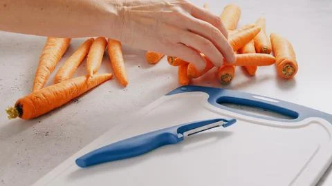 Woman's hands peeling carrots using a peeler knife Stock Photos