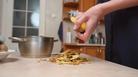 Woman's hands peeling potatoes with a vegetable peeler in the kitchen Stock Footage 328589511