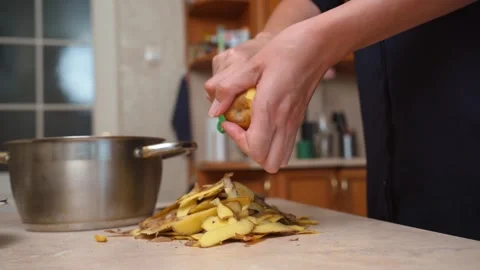 Woman's hands peeling potatoes with a vegetable peeler in the kitchen Stock Footage 328589543