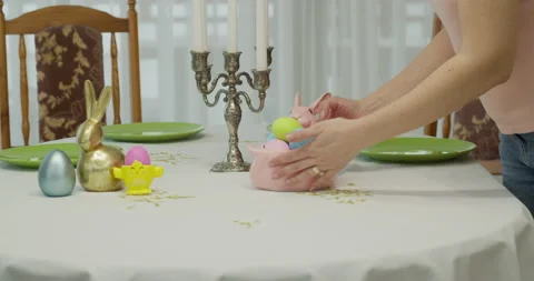 Woman's hands place a pink rabbit-shaped bowl with colored eggs on the table Stock Footage