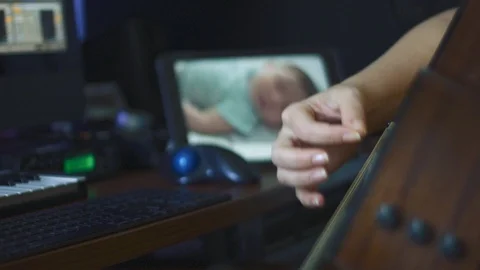 Woman's hands playing guitar and checking baby through monitor Stock Footage 113940227