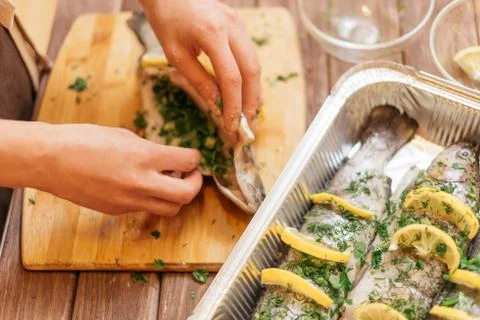 Womans hands preparing fish with greenery. Stock Photos
