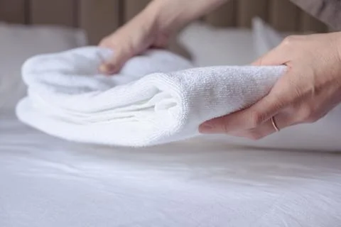 Woman's hands puts a clean white terry towel on the bed Stock Photos