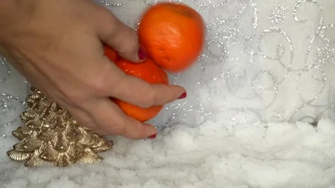 Woman's hands putting orange mandarins on an artificial white snow on a Stock Footage 256066331