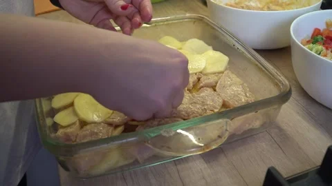 A womans hands with red nails carefully layer sliced potatoes over seasoned Stock Footage 322900384