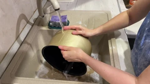 Womans hands rinse a clean non-stick multicooker bowl and a spatula under Stock Footage 316899739