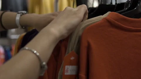 Woman's hands run across a rack of clothes, browsing in a boutique. Stock Footage 99261511