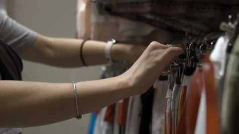 Woman's hands run across a rack of clothes, browsing in a boutique. Stock Footage 99261536