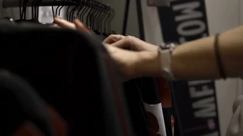 Woman's hands run across a rack of clothes, browsing in a boutique. Stock Footage 99261540