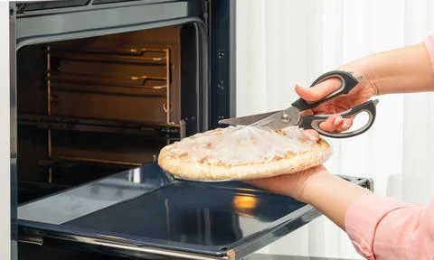 Woman's hands with scissors cut a package of pizza close-up Foto stock