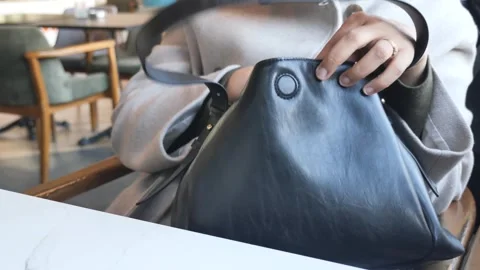 Woman's hands searching inside black leather handbag with strap in cafe. Vídeo Stock 331934609