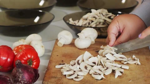A woman's hands slice champignons on a cutting board and toss them into a p.. Vidéo 331664242