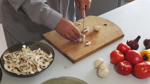 A woman's hands slice champignons on a table with vegetables. Medium shot. Video stock 321439214