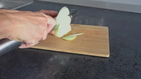 A woman's hands slice an onion into half rings with a knife on a wooden board. Stock Footage 336594897