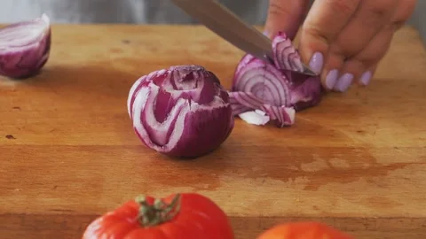 A woman's hands slice red onions on a table with vegetables. Medium shot. Stock Footage 340472726